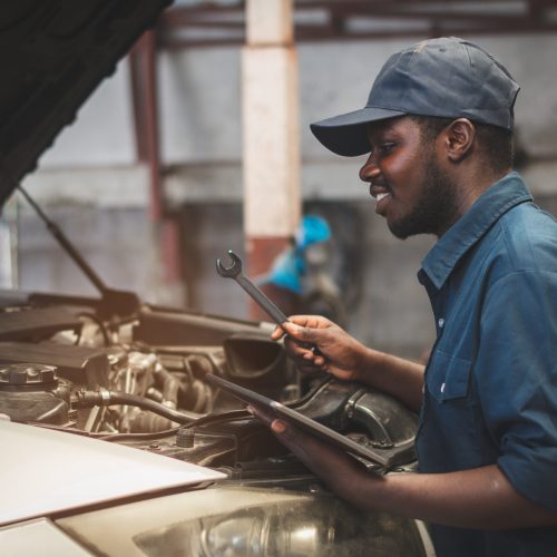 African maintenance male checking car with use wrench and tablet , service via insurance system at Auomobile repair and check up center